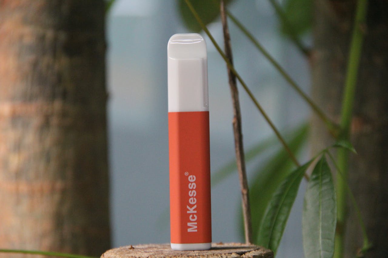 Orange and white vape pen displayed outdoors against trees and leaves