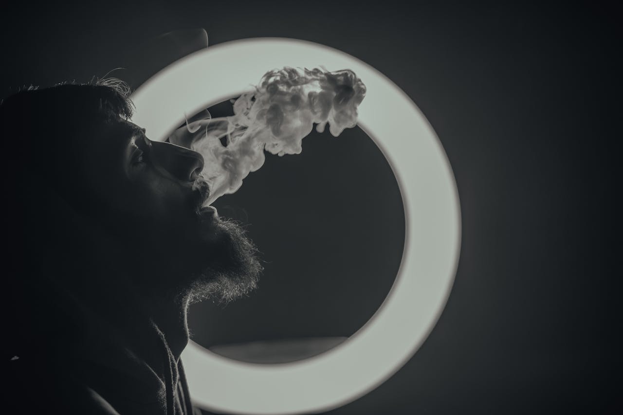Artistic black and white image of a man exhaling smoke against a circular light backdrop.