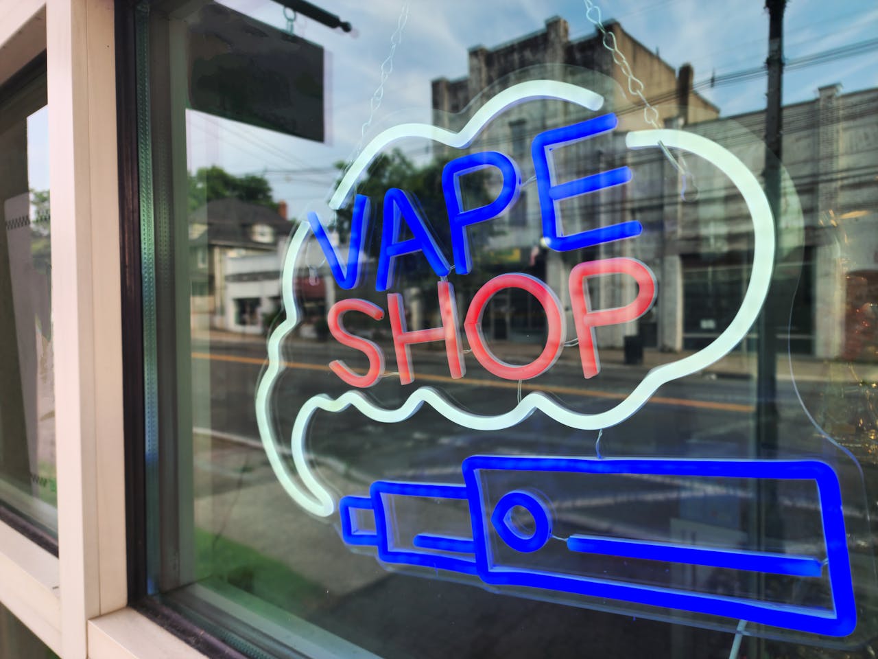 Home Bright neon sign of a vape shop in a city window reflecting the urban street.